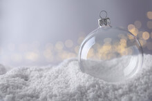 Transparent Christmas Ball On Snow Against Blurred Fairy Lights, Space For Text