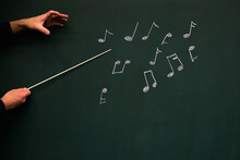 Cropped Hands Holding Stick At Chalk Drawing Of Musical Notes On Black Background