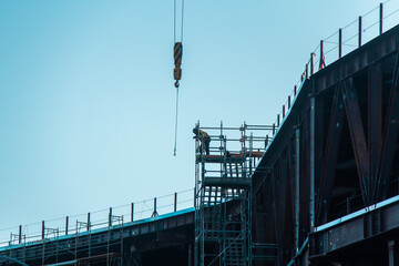 A lone, silhouetted worker leaning over the rail on tall construction site with a crane in front of him 
