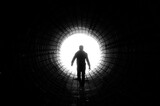 Fototapeta Perspektywa 3d - Silhouette of a man walking to the light at the end of a big tunnel. Concept of escape, exit, freedom, clinical death
