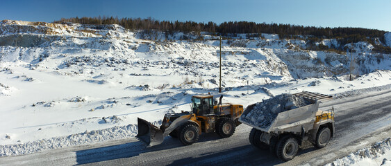 Wall Mural - Heavy mining truck and front-end loader against the backdrop of a snow-covered stone quarry, panorama.