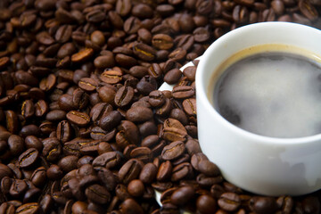 Close-up of coffee cup with roasted coffee beans surrounded by coffee beans