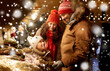 © Syda Productions - family, winter holidays and celebration concept - happy mother, father and little daughter buing wreath at christmas market on town hall square in tallinn, estonia over snow