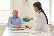© Studio Romantic - Senior patient consulting young doctor sitting at desk in modern hospital office