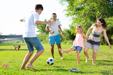 Wall Mural - Group of smiling children and parents having fun together outdoors playing football. High quality photo