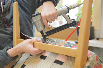 Wall Mural - Making new upholstery on old chair. Woman hands working in upholstery workshop with pneumatic stapler. Finishing new upholstery on chair from 
the sixties. Furniture restoration workshop.