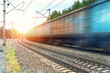 Motion blurred heavy cargo freight rusty train wagons moving on railway on sunset or sunrise day time. Industrial materials transportation and goods delivery concept. Old rusty wagons moving by rail