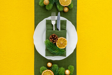 Table setting with spruce, plate, flatware on yellow background top view