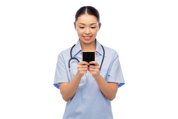 Wall Mural - medicine, profession and healthcare concept - happy smiling asian female doctor or nurse in blue uniform with stethoscope using smartphone over white background