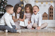 © Evia_Art - Merry Christmas card. Four happy kids sitting near fireplace, boys and girls opening giftbox. Children new year party invitation. Birthday card