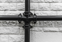 Old Fashioned Heavy Cast Iron Black Drainpipes Against A White Brick Wall.