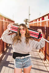 Wall Mural - Urban portrait of a young skater woman holding a longboard skateboard.