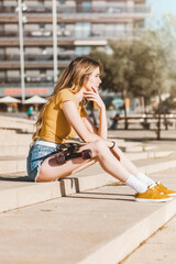 Wall Mural - Long board girl sitting on the stairs outdoors with a skateboard in summer. Sunny day for outside activities. Cool California concept