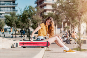 Wall Mural - Long board girl sitting on the stairs outdoors with a skateboard in summer. Sunny day for outside activities. Cool California concept