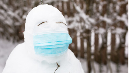 Snowman in a medical mask - a new reality, protection from disease, infection, life in the covid epidemic. Women's hands put on a snowman mask. Winter family outdoor activities