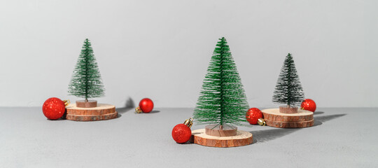 Conceptual festive composition with miniature Christmas trees on wooden podiums and red xmas decorations