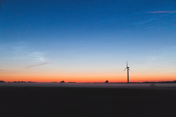 wind turbine at sunset and fog over a field