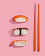 Sushis or nigiris with orange chopsticks over a pink background