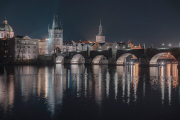 
illuminated Charles Bridge from 14 centuries and light from street lighting and stone sculptures on the bridge and light reflections on the surface of the Vltava river at night in Prague