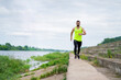 © Georgii - Athletic jogging asian man in stylish sportswear on workout outside in cloudy weather on embankment