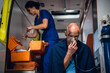 © Anna Kosolapova - A medical worker preparing a dropping tube, a man with an oxygen mask on in the foreground.