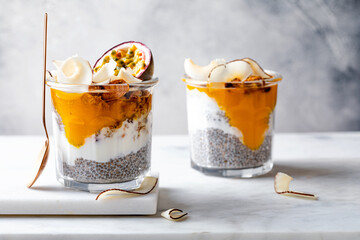 Healthy tropical fruit chia pudding with granola, mango, passion fruit and coconut chips in a glass jar. Vegan healthy breakfast, clean eating.