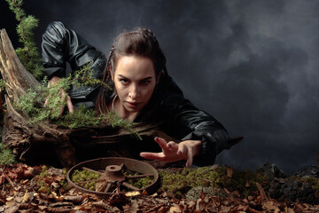 A young woman in a black leather jacket climbs out of the pit holding on to a snag.