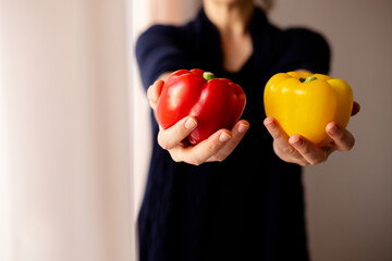 Woman holding fresh red and yellow pepper in front of her body and close to camera