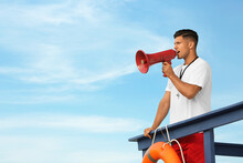 Male Lifeguard With Megaphone On Watch Tower Against Blue Sky
