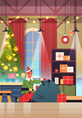 Wall Mural - green elf boy santa claus helper with sack full of gifts happy new year merry christmas holidays celebration concept workshop interior full length vertical vector illustration