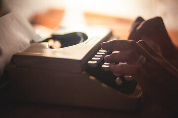 Fototapete - Process of writing a text letter on a white sheet of paper with old-fashioned typewriter, modern writer machine in warm room light, close up view of hands writing and printing