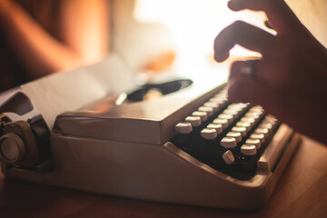 Fototapete - Process of writing a text letter on a white sheet of paper with old-fashioned typewriter, modern writer machine in warm room light, close up view of hands writing and printing