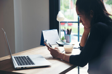 Wall Mural - Remote working at Home office Concept. Businesswoman working online via smartphone. Asian young entrepreneur watching webinars and talking during meeting video conferences calls with team