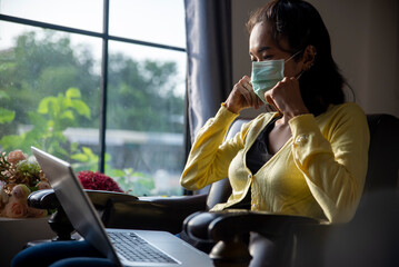 Wall Mural - Remote working at Home office Concept. Businesswoman  mask and working online via laptop. Asian young entrepreneur watching webinars and talking during meeting video conferences calls with teamwork.