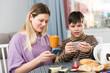 © JackF - Portrait of young mother and son using phones during breakfast indoors