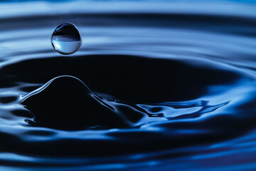 Dark blue water droplets splashed closely on the water surface. It creates a water wave and a perfect crown.