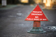 Shallow-focus close-up of a red triangular sign depicting restricted access to the foreground and soft-focus gravel road to the background.