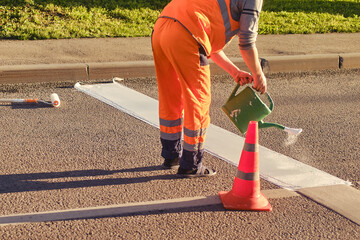 A road worker draws a stop line on the asphalt with white paint using a watering can