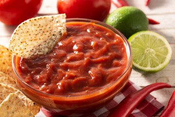 Spicy chili sauce in bowl with nacho chips on wooden table	