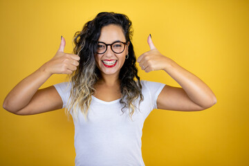 Young beautiful woman wearing casual white t-shirt over isolated yellow background smiling and doing the ok signal with her thumbs