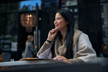 Beautiful joyful woman sitting at the table in outdoor cafe