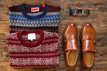 Wall Mural - Top view shot of folded sweater with festive pattern and brown men's shoes. Set of male clothing. Close up, copy space, flat lay, background.