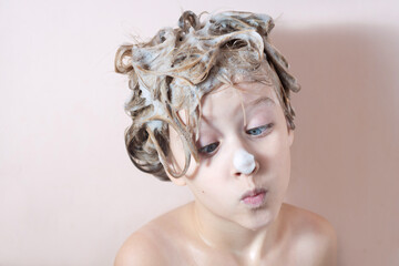 Wall Mural - a little blonde girl washes her hair in the shower with foam on her hair and nose. playing in the ba
