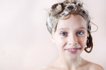 Wall Mural - a little blonde girl with a soapy head smiles in the bathroom on a pink background