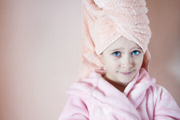 Wall Mural - a little girl with blue eyes in a pink robe and a pink towel on her head after a bath smiles and loo