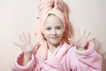 Wall Mural - a little girl with blue eyes in a pink robe and a pink towel on her head after a bath smiles, looks 
