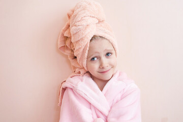 Wall Mural - a little girl with blue eyes in a pink robe and a pink towel on her head after a bath smiles and loo