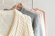 Bunch of knitted warm pastel color sweaters with different vertical knitting patterns hanging on the rack, clearly visible texture. Stylish fall / winter season knitwear clothing. Close up, copy space