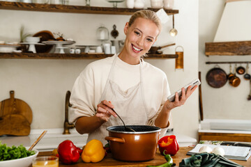 Poster - Beautiful woman smiling and using cellphone while making lunch