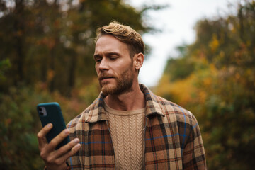 handsome man using mobile phone while strolling in autumn forest
